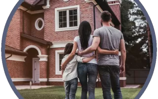 Family standing in street looking at brick home with new roof installed by a residential roofing company.