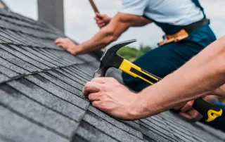 roofers hammering shingles onto roof