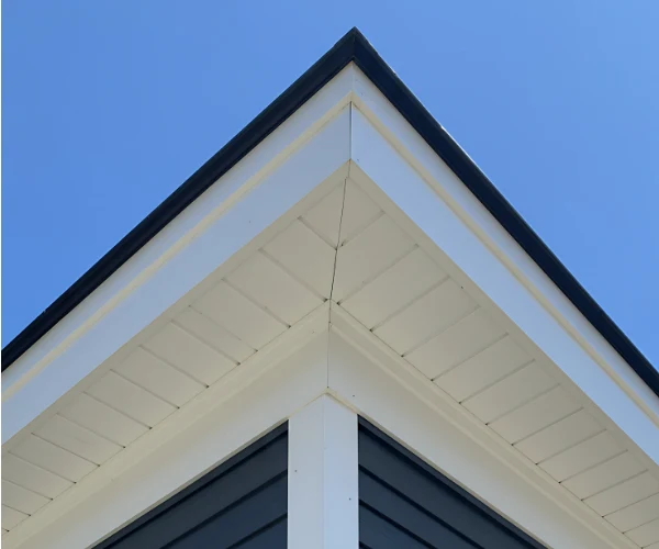 The sharp corner of a modern house roof with white trim and blue siding, set against a clear blue sky.