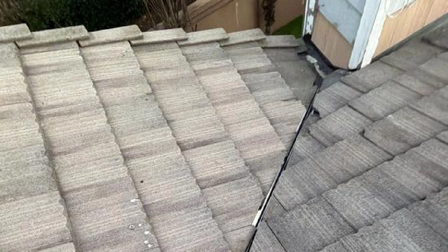 A roof with overlapping gray tiles, maintained for Tile Roof Leak Repair & Maintenance in Pleasanton, features a black cable running diagonally near a small structure with light blue siding.