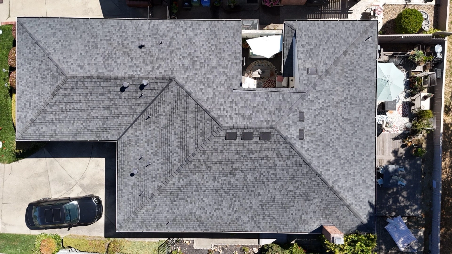 Aerial view of a house featuring a gray shingled roof, recently updated through re-roofing with new sheathing in Danville; a car is parked in the driveway, and patios with outdoor furniture are arranged in the backyard.